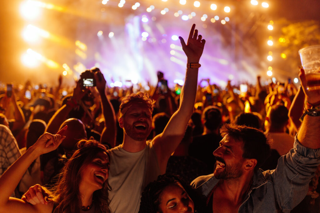 Group of young friends partying and celebrating at summer music festival. They are dancing in front of stage. Wearing casual clothing