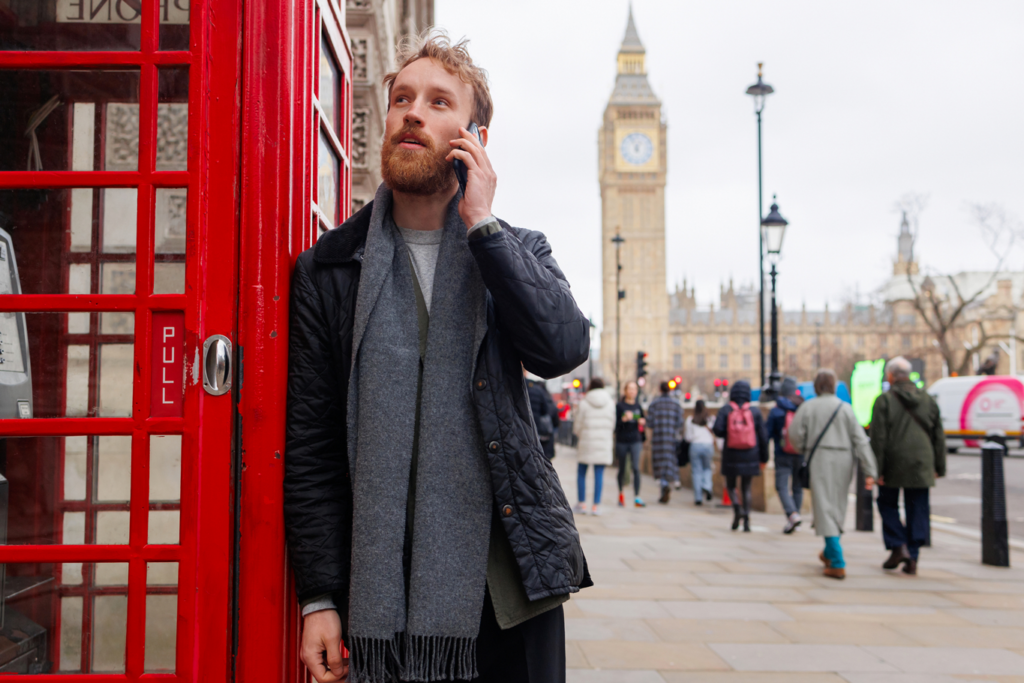 Smartly dressed man on phone in London leaning on red phone box