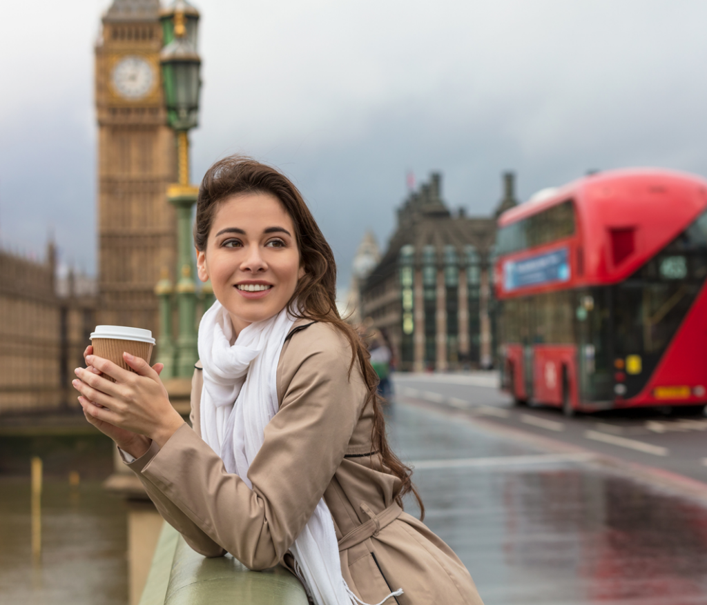 Smartly dressed lady with coffee on River Thames bridge in London United Kingdom. Big ben and red bus in background.