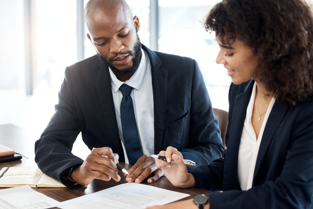 A man and woman in business attire collaborate on paperwork at a desk, focused on their tasks.