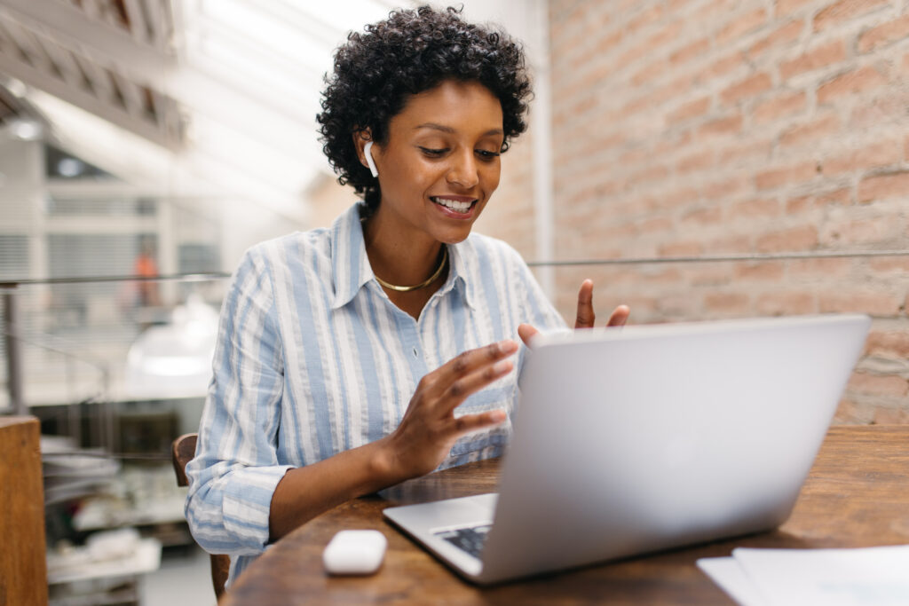 Ethnic small business owner having an online meeting in a warehouse. Female entrepreneur video calling her business partners on a laptop. Happy businesswoman running an online startup.