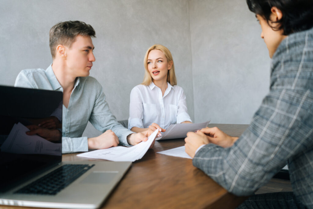 Low-angle view of serious HR managers advisors interviewing young male in office. Employers holding curriculum vitae talk about applicant guy. Disbelief dissatisfied, bad first impression concept