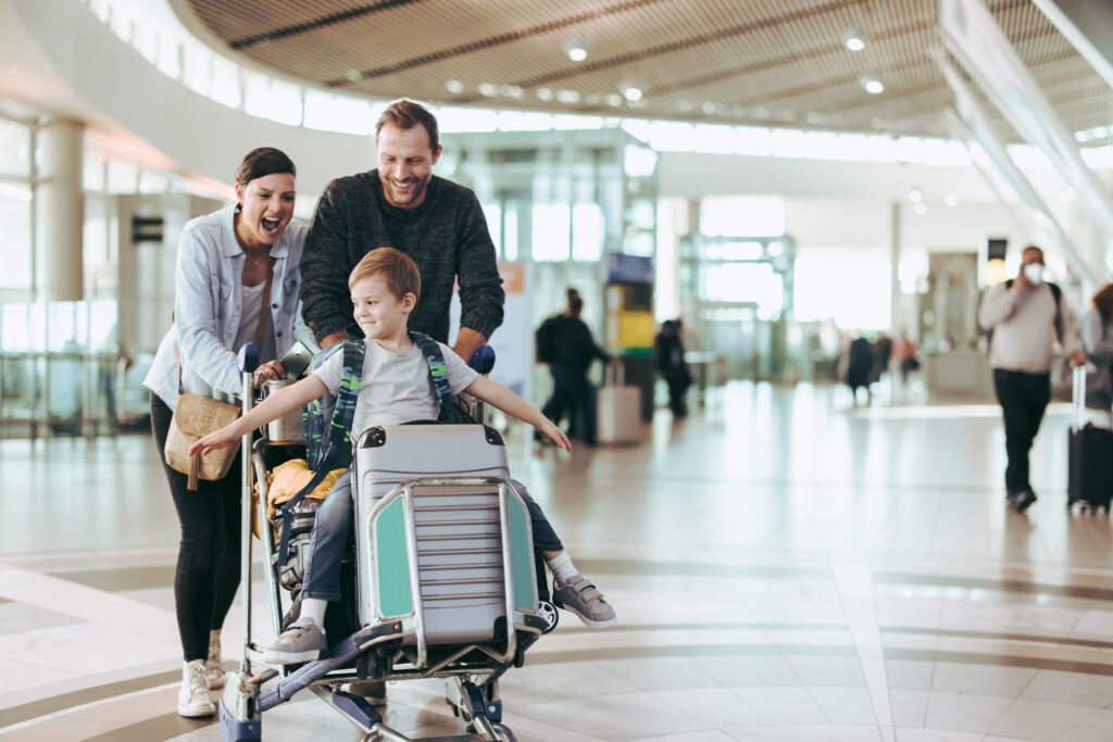 Couple happily pushing the trolley with their son at airport. Child enjoying sitting on luggage trolley while parents pushing it at airport travel