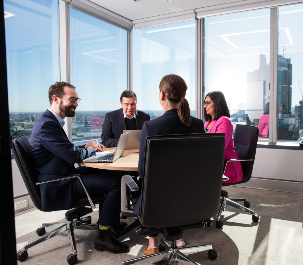 four people in meeting room at round table working and smiling