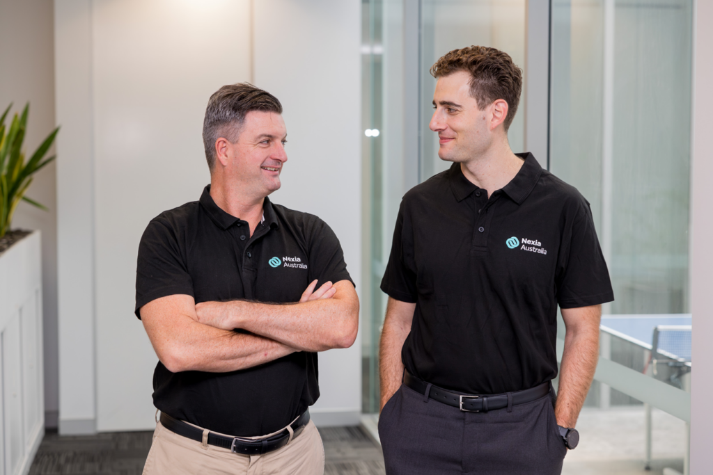 Two men wearing black shirts standing in an office environment.